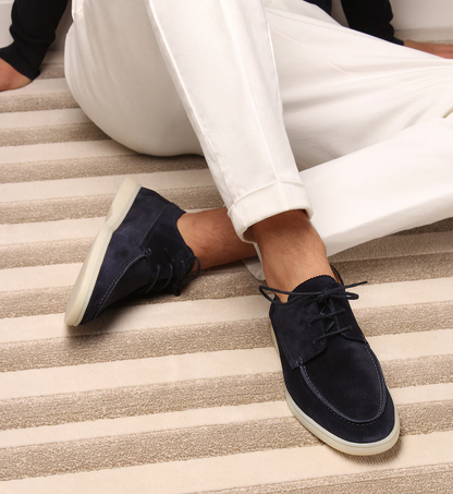 Dunkelblaue Wildleder-Sneaker für Herren, kombiniert mit weißen Hosen auf gestreiftem Teppich.
