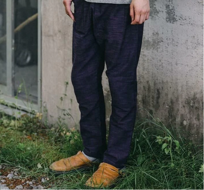 Mann trägt dunkelblaue Leinenhose, braune Lederschuhe, steht auf Gras vor Betonwand.