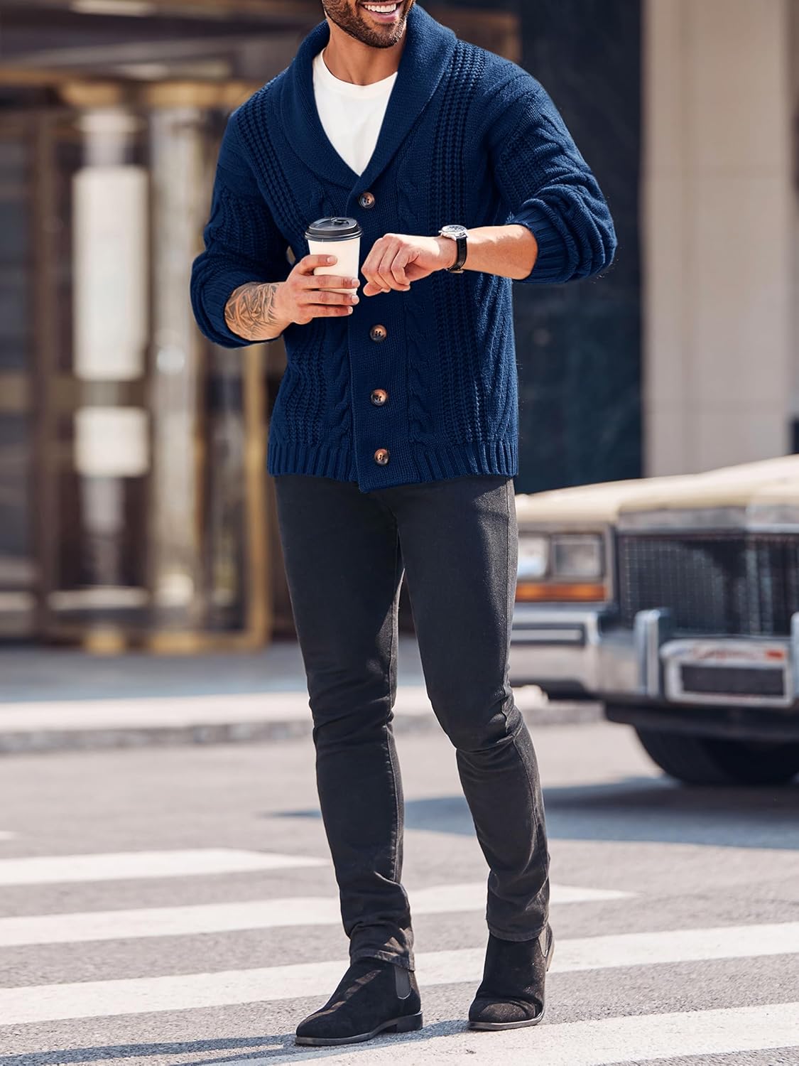 Mann in dunkelblauer Strickjacke mit Kaffeebecher, schwarze Hose, auf Straße gehend.