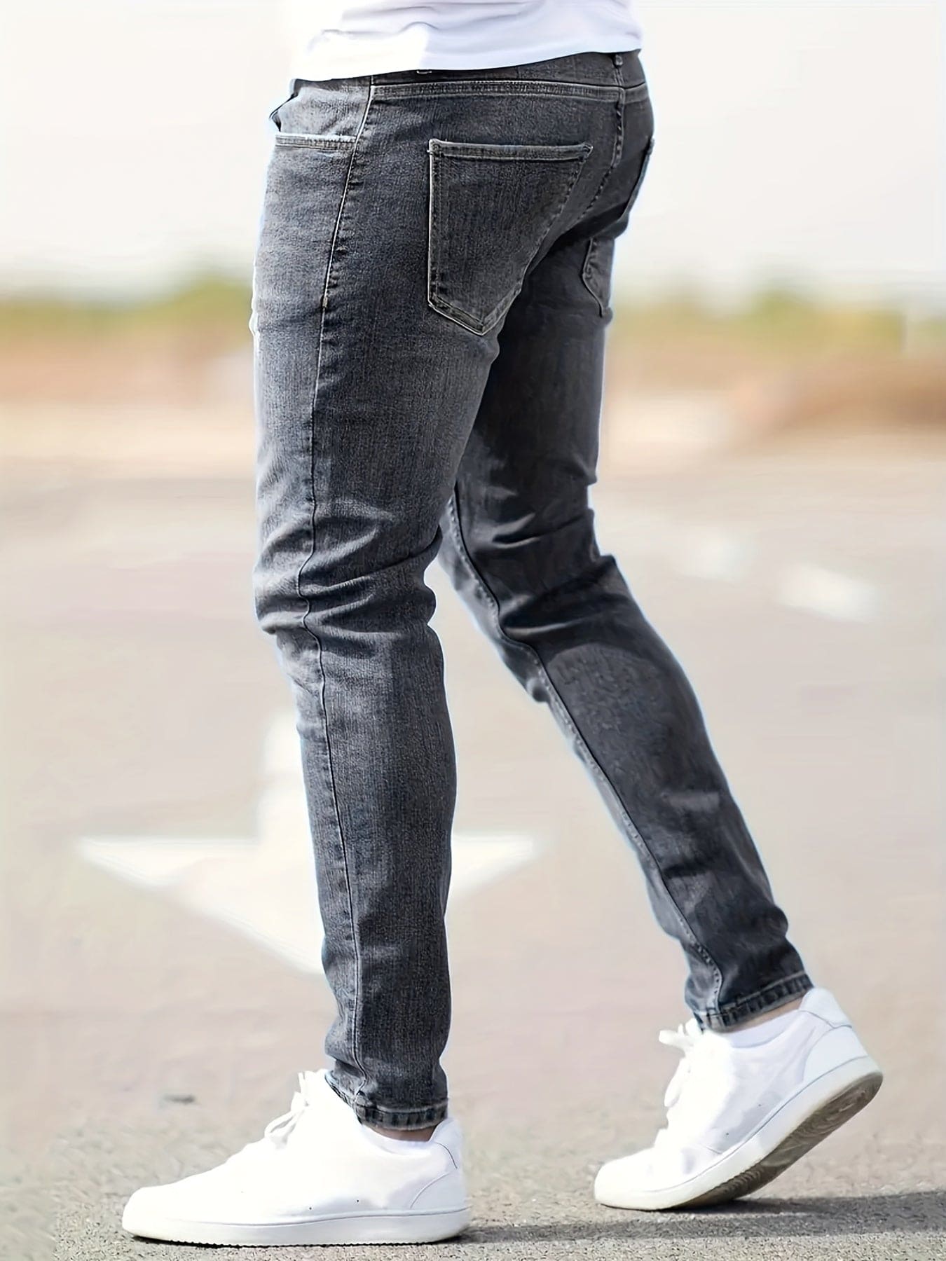 Mann in grauer Slim-Fit-Jeans und weißen Sneakers auf Straße, lässige Herrenmode.