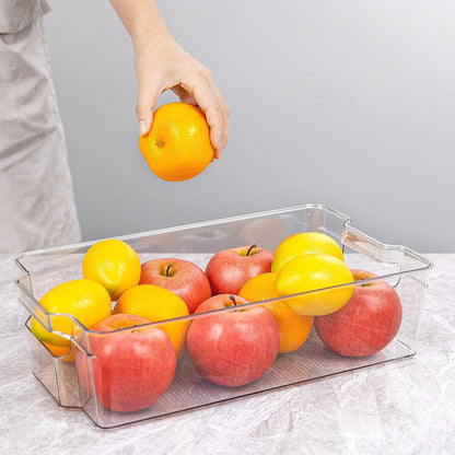 Hand legt Orange in transparenten Kunststoffbehälter mit Äpfeln und Zitronen auf Marmoroberfläche.