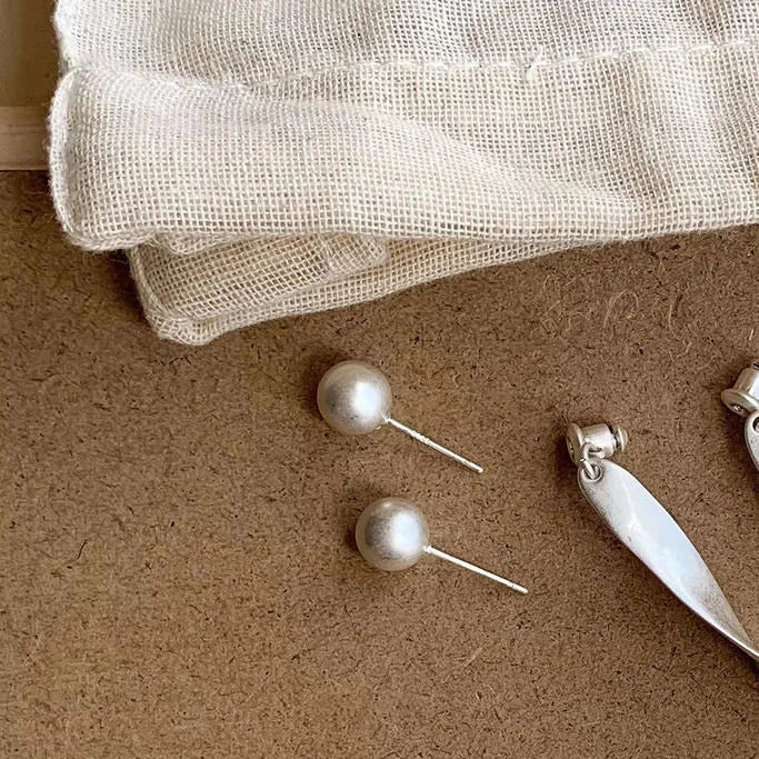 Silberne Perlenohrringe auf beigem Stoff, eleganter Schmuck, minimalistisch, zeitloses Design.