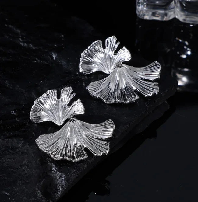 Silberne Ginkgo-Ohrringe auf schwarzem Hintergrund, eleganter Schmuck, modisches Accessoire.
