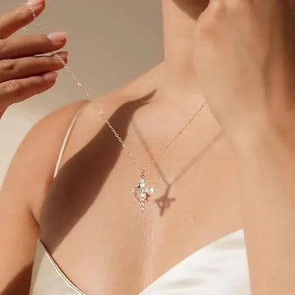 Kvinna i vit topp håller upp ett fint halsband med korshänge och glittrande stenar mot sin hals, med skugga på huden. 1