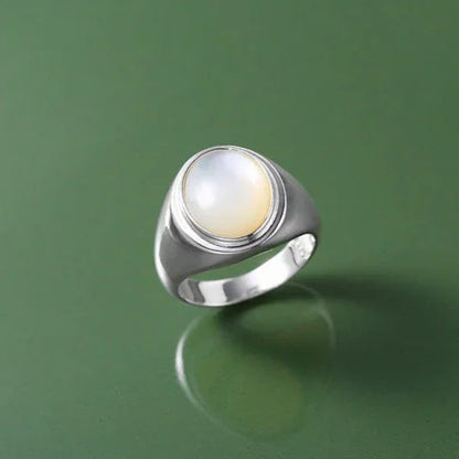 Silberring mit rundem Mondstein auf grünem Hintergrund, elegantes Schmuckdesign.
