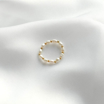 Echter Perlenring auf weißem Stoff, eleganter Schmuck, zeitloses Design, Damenaccessoire.