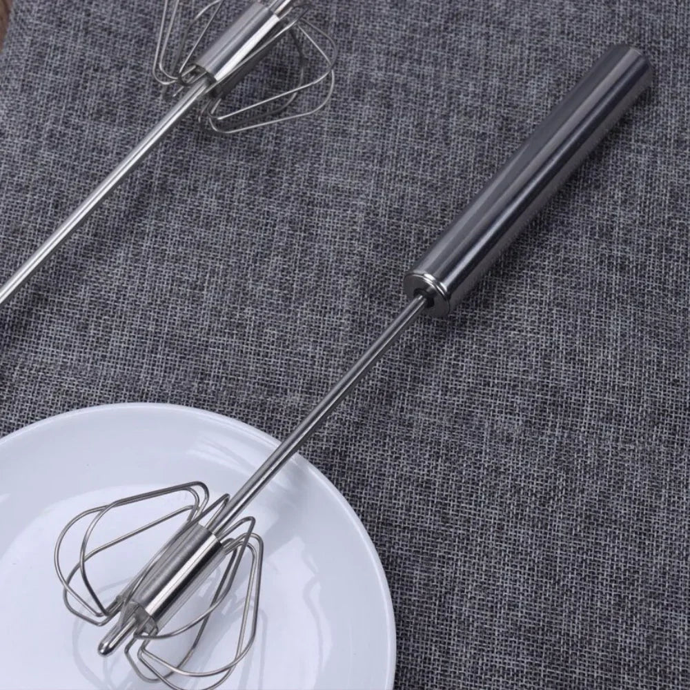 Edelstahl Handmixer auf grauem Stoff, neben weißem Teller, Küchengerät, langlebig, modern.