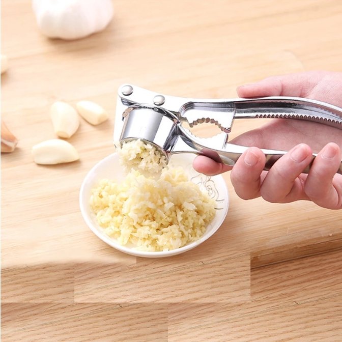 Edelstahl Knoblauchpresse, manuell, auf Holzbrett, mit gehacktem Knoblauch, Küchenwerkzeug.