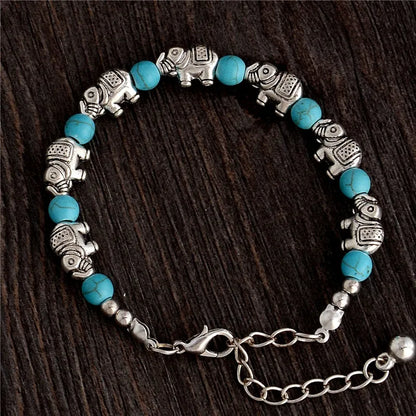 Silberarmband mit türkisfarbenen Perlen und Elefantenanhängern auf dunklem Holz.