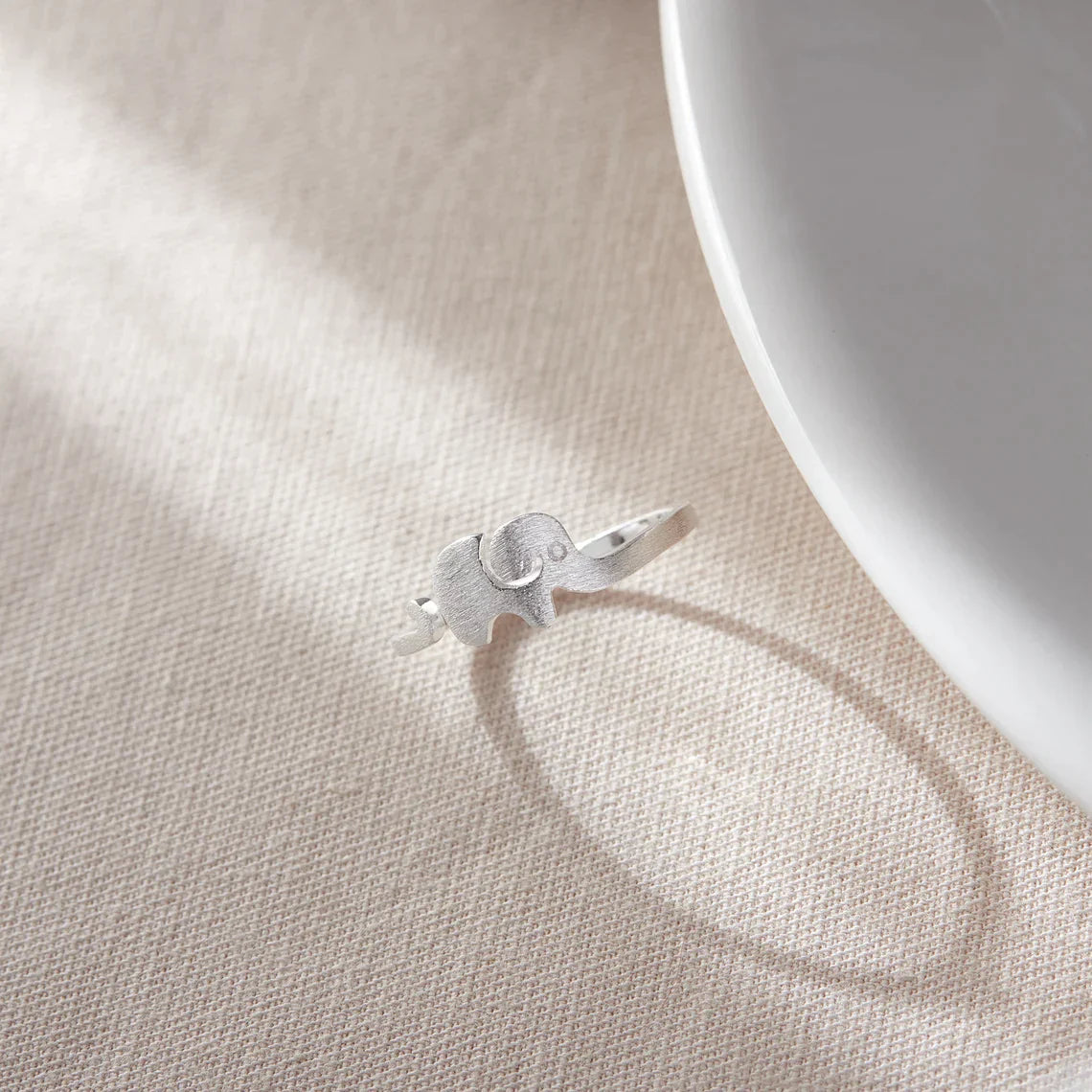 Silberner Elefantenring auf beigem Stoff, eleganter Schmuck, Tiermotiv, Geschenkidee.