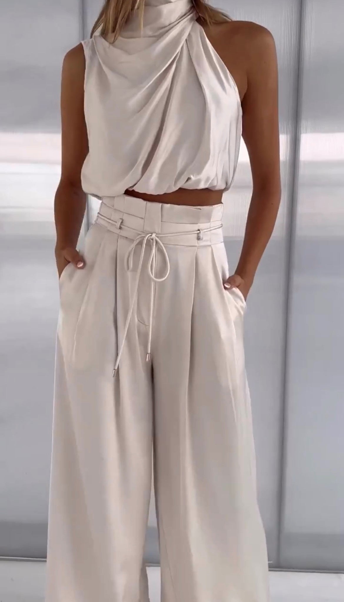 Damen-Outfit aus cremefarbenem Satin, ärmelloses Oberteil und weite Hose, elegant und modern.