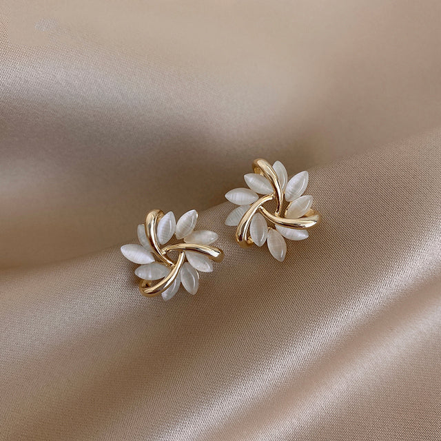 Elegante goldene Ohrringe mit weißen Blütenblättern auf beigem Stoff, klassischer Schmuck.