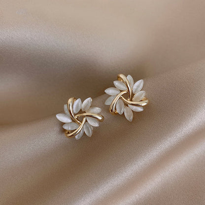 Elegante goldene Ohrringe mit weißen Blütenblättern auf beigem Stoff, klassischer Schmuck.