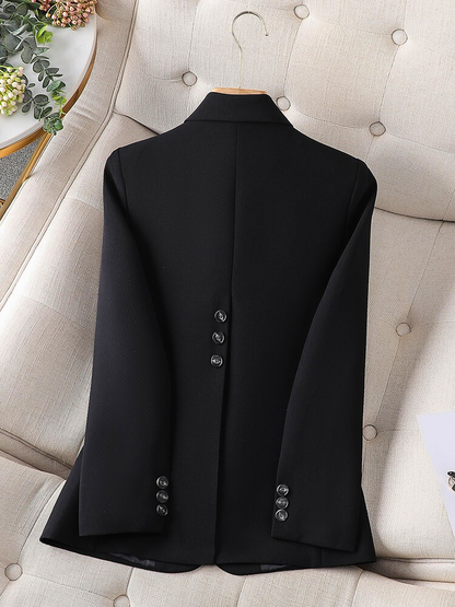 Schwarzer Blazer aus Wolle, Rückansicht, elegante Knöpfe, auf beigem Sessel drapiert.