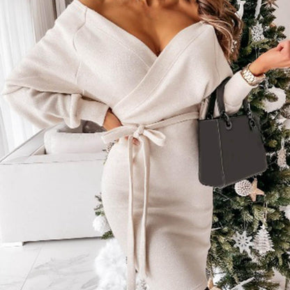 Frau in cremefarbenem Wickelkleid mit Gürtel, schwarze Handtasche, elegantes Outfit, Wohnzimmer.