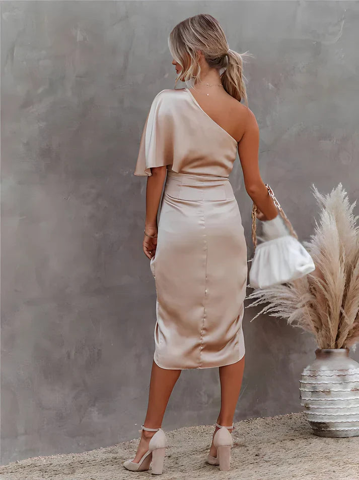 Frau in eleganter, einseitiger, beiger Satin-Kleid, hält weiße Handtasche, steht vor Pampasgras.
