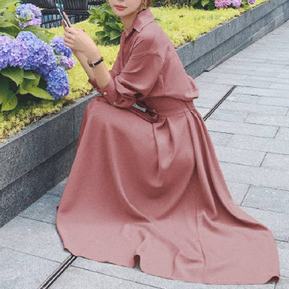 Frau in rosa Maxikleid sitzt neben Hortensien im Garten, elegantes Sommeroutfit.