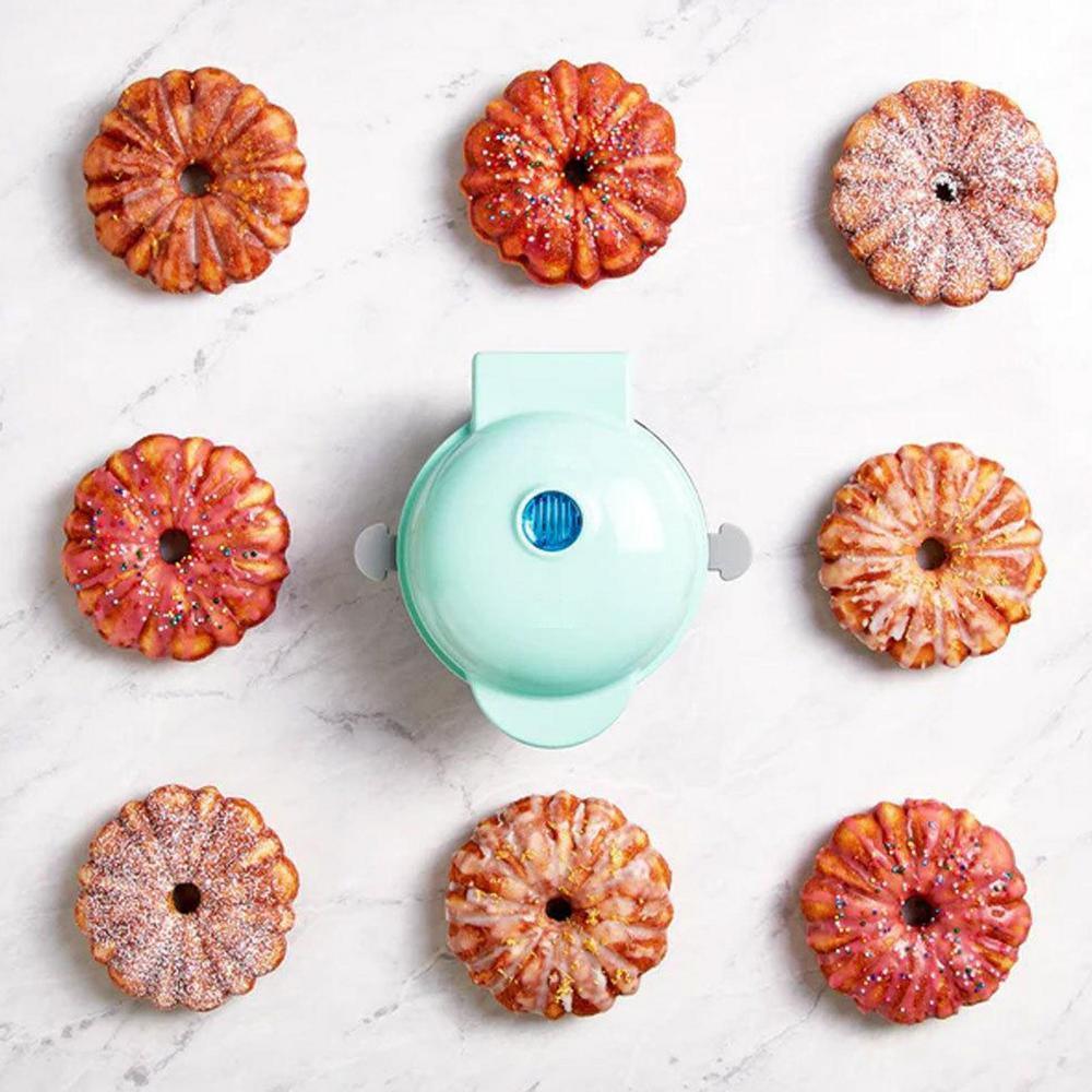 Tragbare elektrische Kuchenmaschine in Mintgrün mit sieben gebackenen Donuts auf Marmorhintergrund.