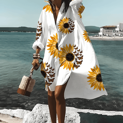 Frau im weißen knielangen Kleid mit Sonnenblumenmuster am Strand.