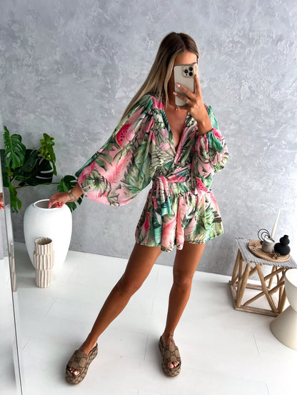 Frau in grün-rosa Sommerkleid mit tropischem Muster, steht in modernem Raum.