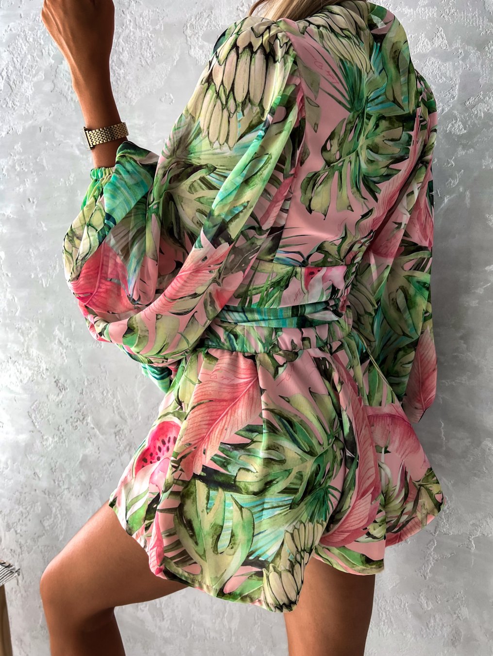Frau in grün-rosa tropischem Kleid, lange Ärmel, Gürtel, Sommermode, floral, elegant.