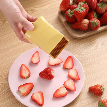 Gelber Obstschneider für Erdbeeren, handgehalten, auf Holztisch mit geschnittenen Erdbeeren.