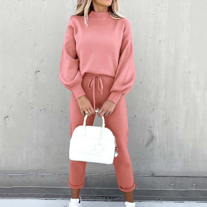 Frau in rosa Strickpullover und Hose, hält weiße Handtasche, modisch, lässig, Herbstmode.