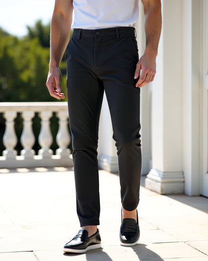 Mörkgrå chinos med vit t-shirt och svarta loafers, stylade på en solig terrass med vita pelare och balustrad. 7