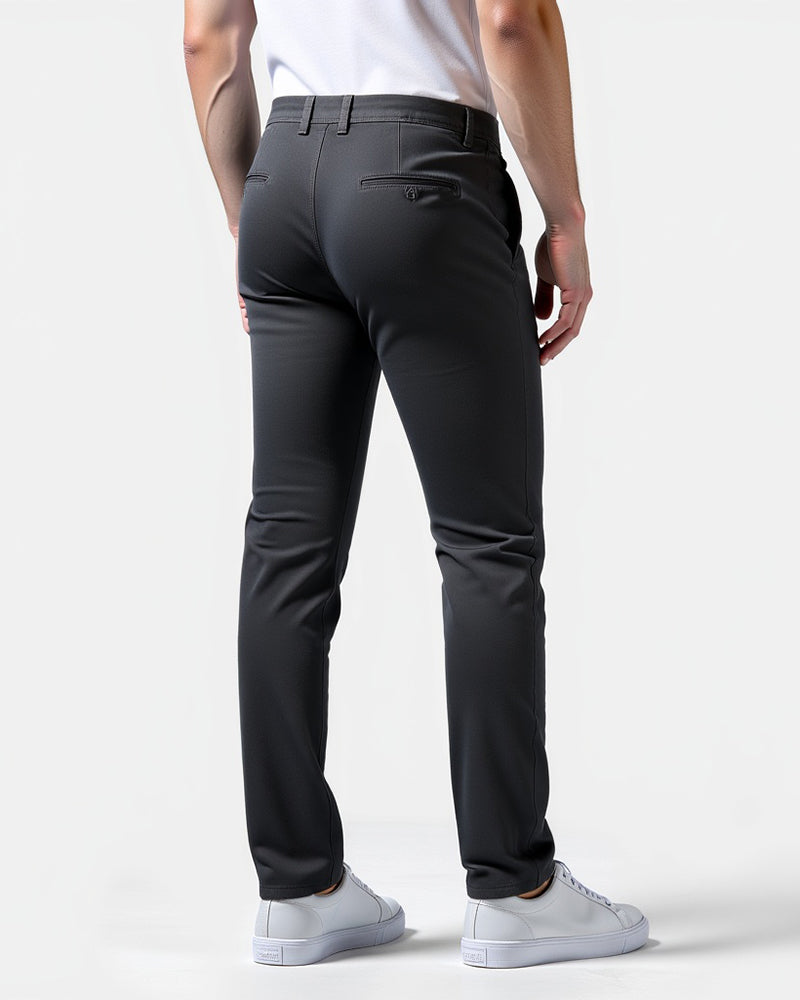 Mörkgrå chinos sedda bakifrån på en modell, med knäppt bakficka, skärphällor och vita sneakers. 8