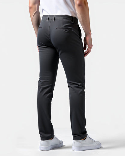 Mörkgrå chinos sedda bakifrån på en modell, med knäppt bakficka, skärphällor och vita sneakers. 8