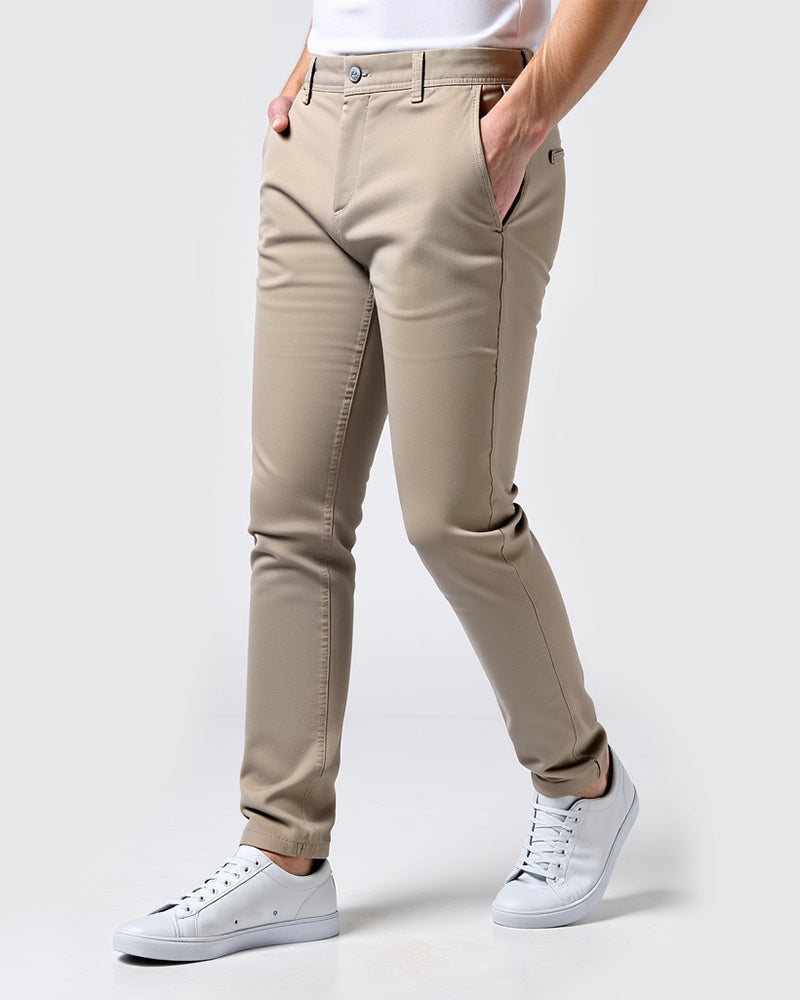 Beige chinos snett framifrån på en modell med vit t-shirt och vita sneakers, handen i fickan och uppvikta byxben. 14