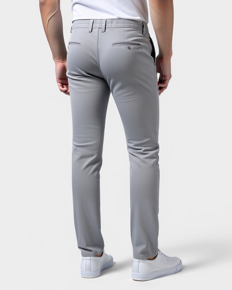 Ljusgrå chinos sedda bakifrån på en modell, med knäppta bakfickor och skärphällor vid midjan. 3