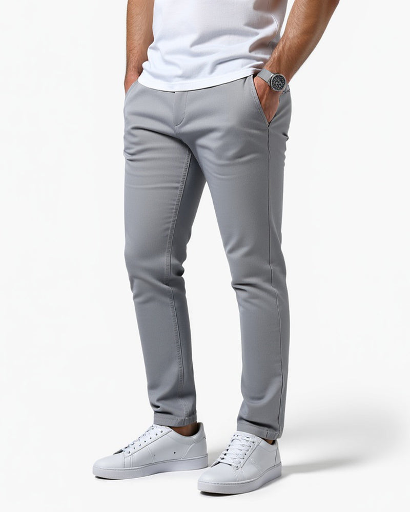 Ljusgrå slim fit-byxor snett framifrån med vit t-shirt och vita sneakers, handen i fickan och armbandsur på handleden. 11