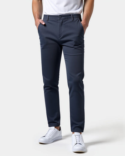 Mörkblå chinos framifrån på en modell med vit t-shirt och vita sneakers, båda händerna i fickorna. 15