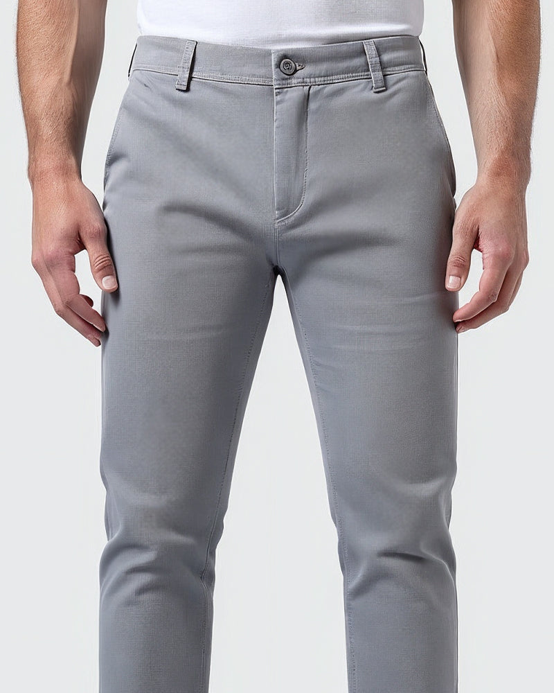 Närbild av ljusgrå chinos framifrån med knäppt midjeband, gylf och skärphällor, bärs av en modell i vit t-shirt. 5