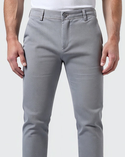 Närbild av ljusgrå chinos framifrån med knäppt midjeband, gylf och skärphällor, bärs av en modell i vit t-shirt. 5