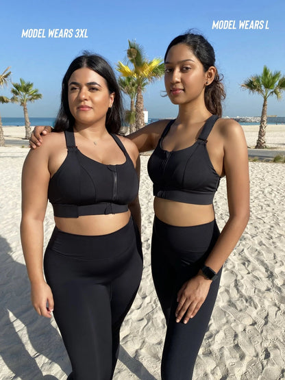 Zwei Frauen in schwarzen Sport-BHs und Leggings am Strand, Palmen im Hintergrund.