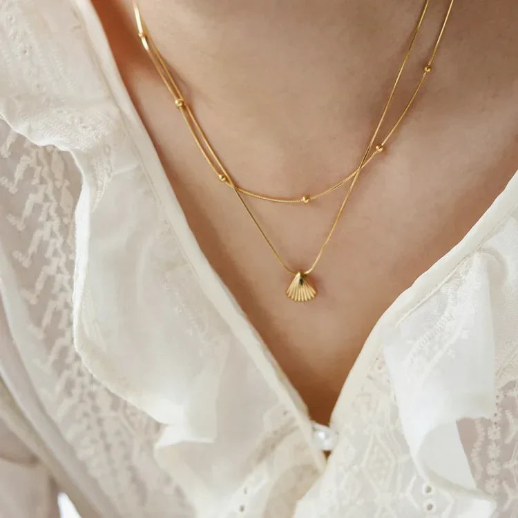 Doppelte goldene Halskette mit Muschel-Anhänger, Damenmode, elegantes Schmuckdesign.