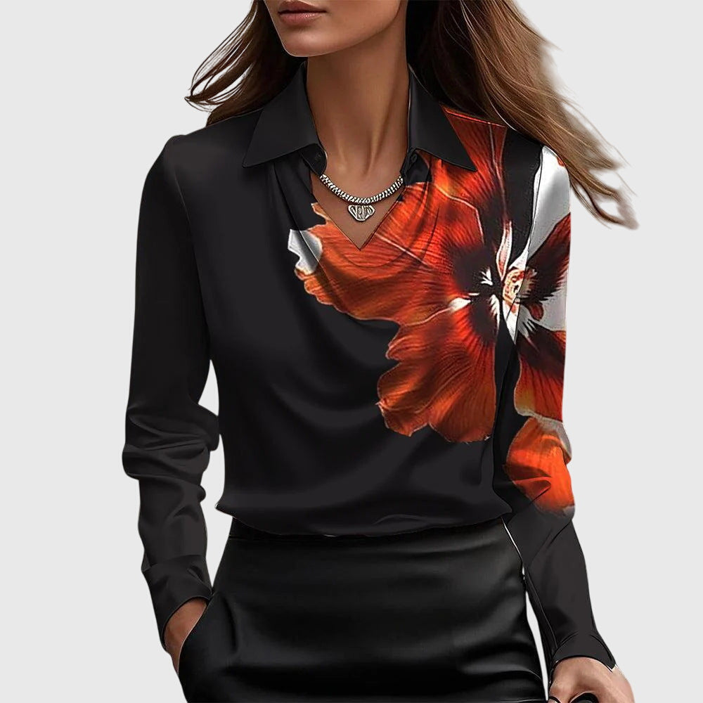 Modell bär svart blus med stor orange blomma på ena axeln, draperad hals och krage, med svart kjol. 6