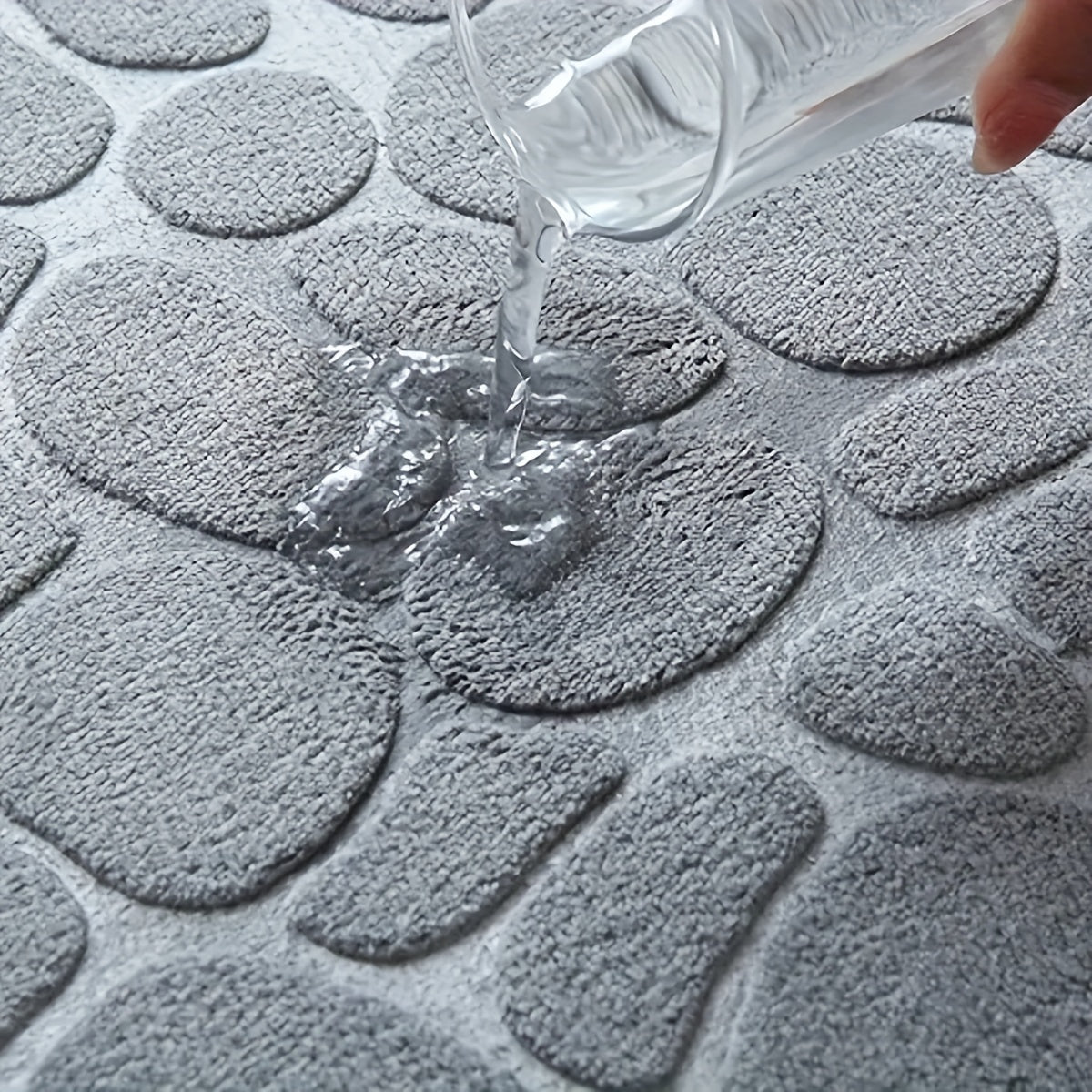 Grauer, wasserabsorbierender Badteppich mit Steinmuster, Wasser wird darauf gegossen.