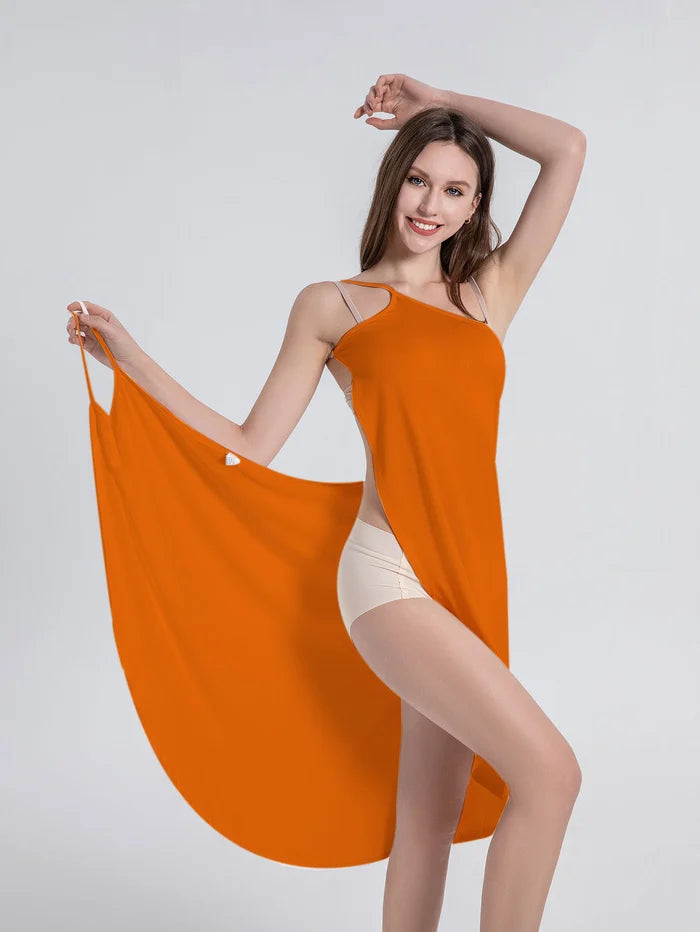 Frau in orangefarbenem Strandkleid, asymmetrisch, Sommermode, lächelnd, grauer Hintergrund.