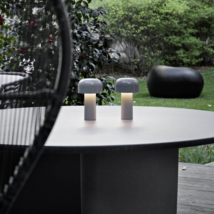Zwei tragbare LED-Tischlampen auf rundem Tisch im Garten, modernes Design, Außenbeleuchtung.