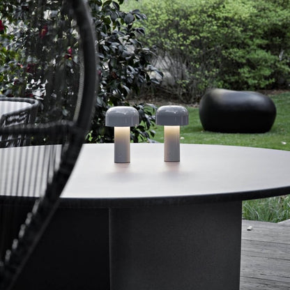 Zwei tragbare LED-Tischlampen auf rundem Tisch im Garten, modernes Design, Außenbeleuchtung.