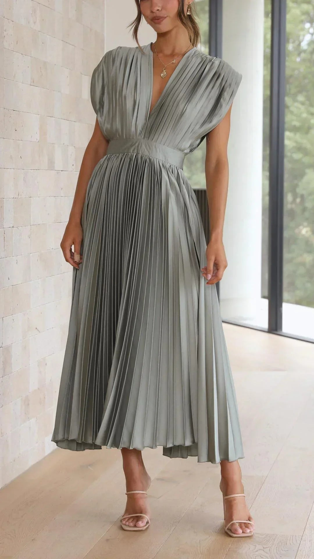 Frau in olivgrünem, plissiertem Maxikleid, elegantes Design, ärmellos, V-Ausschnitt.