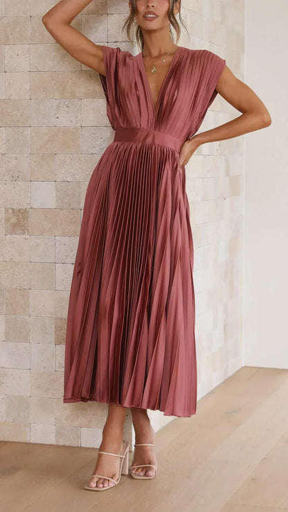 Frau in rotem, plissiertem Maxikleid aus Satin, ärmellos, elegantes Design, vor Steinwand.