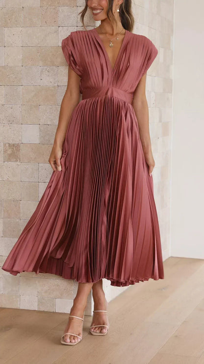 Frau in rotem, plissiertem Maxikleid vor beiger Wand, elegantes Abendmode-Outfit.