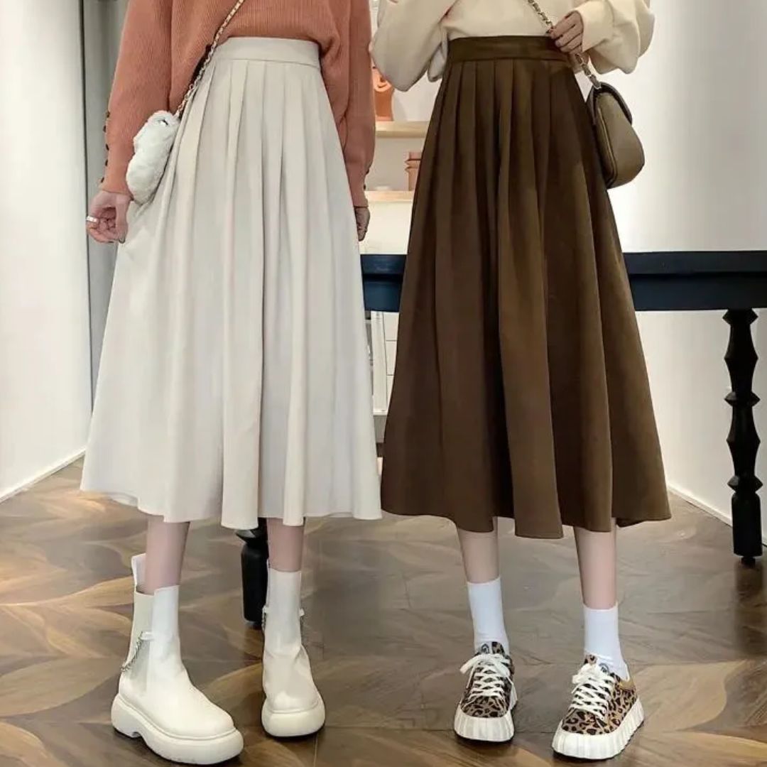 Zwei Frauen in Faltenröcken, beige und braun, mit weißen Stiefeln und Sneakers, modisch gekleidet.