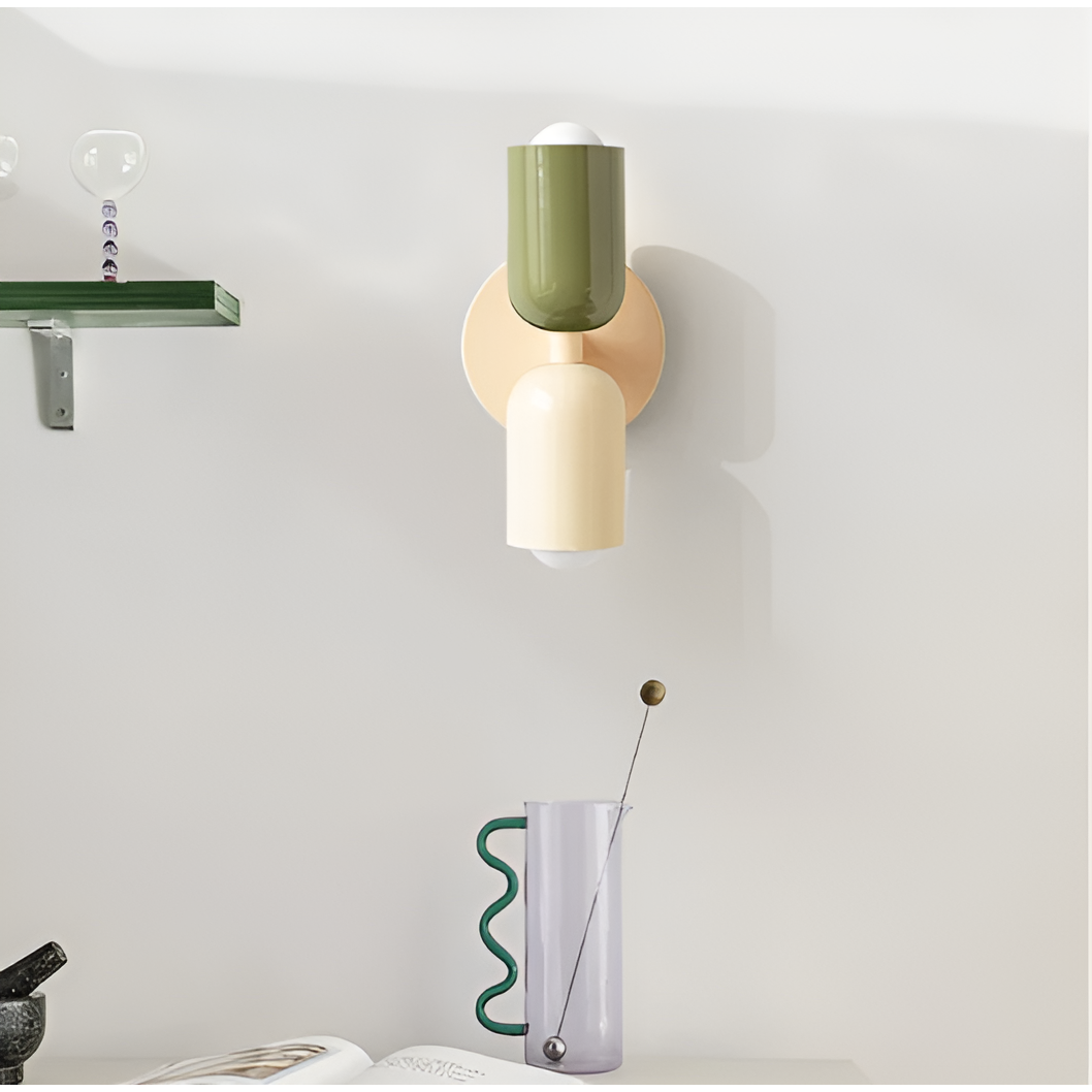 Vägglampa med grön och gräddvit skärm monterad på vägg i ett rum med hylla och glaskaraff. 35