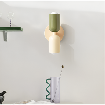 Vägglampa med grön och gräddvit skärm monterad på vägg i ett rum med hylla och glaskaraff. 35