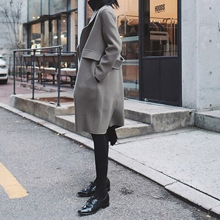 Frau in grauem Wollmantel, schwarze Schuhe, Stadtstraße, modischer Herbst-Look.